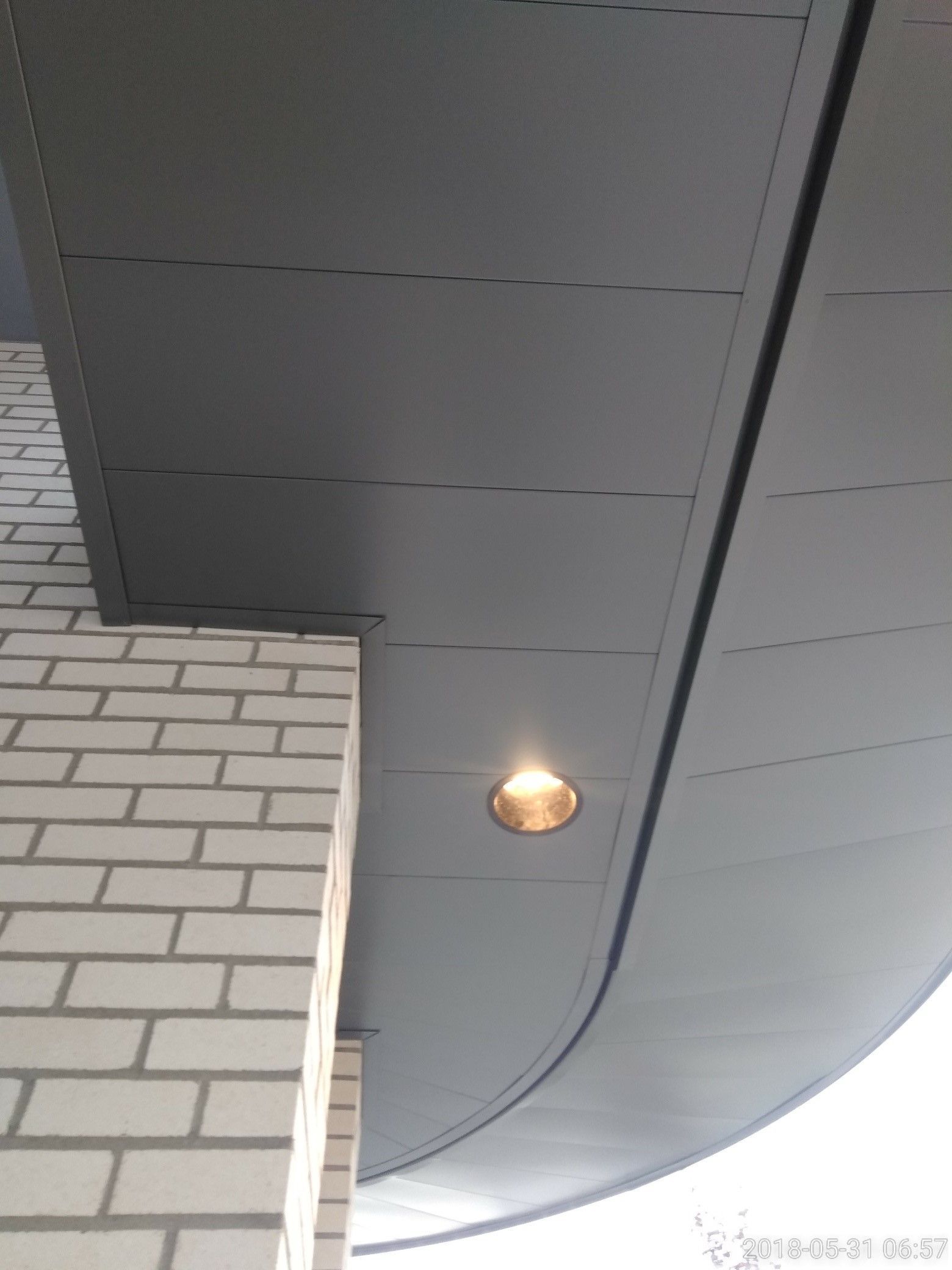 Gray metal panel ceiling with a single recessed light, next to a white brick wall.