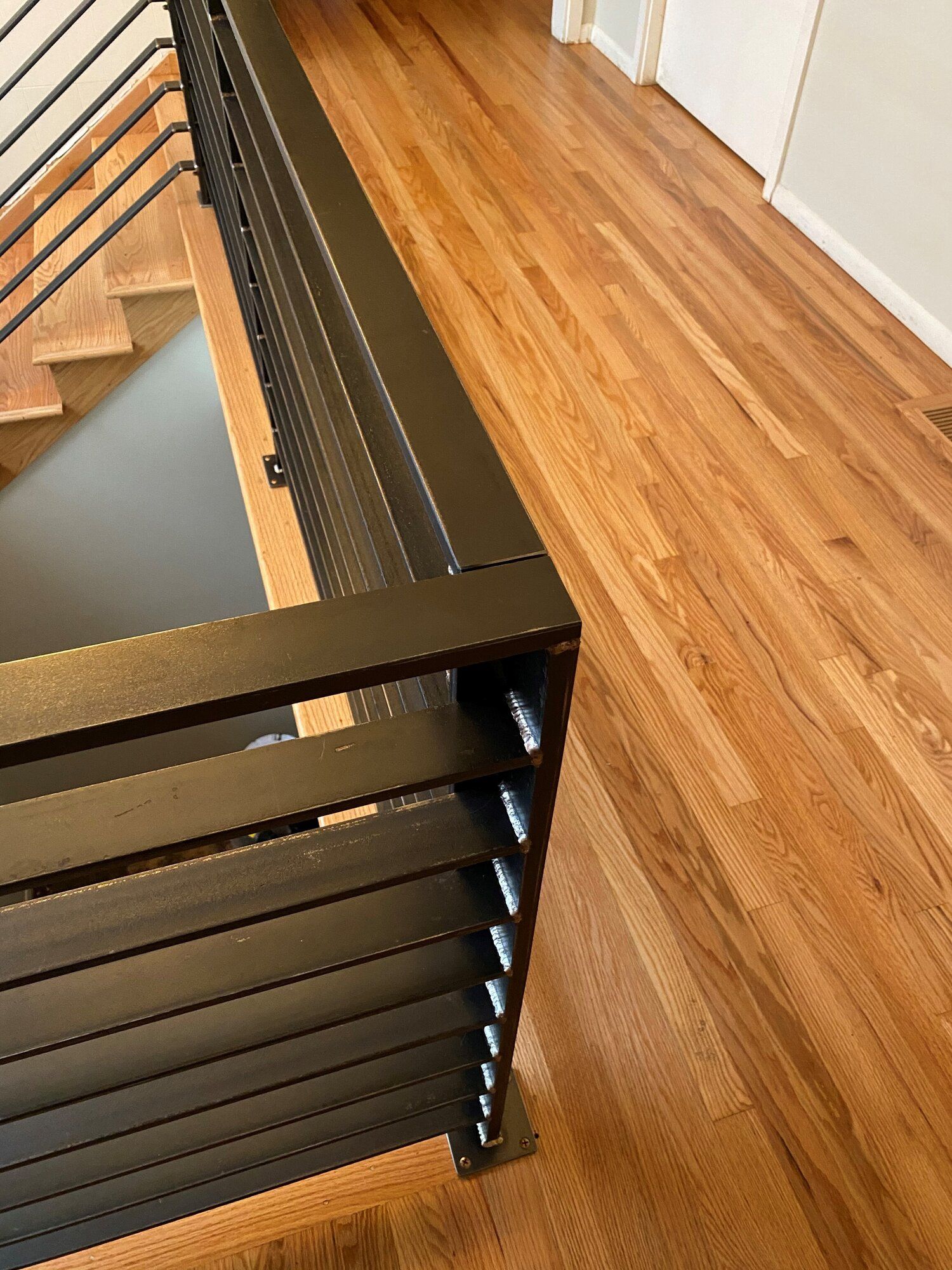 Black metal railing with horizontal slats, on wood floor next to staircase.