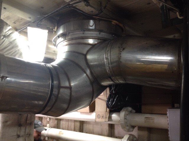 Large, silver metal ductwork branching from a round connection, located in an industrial setting.