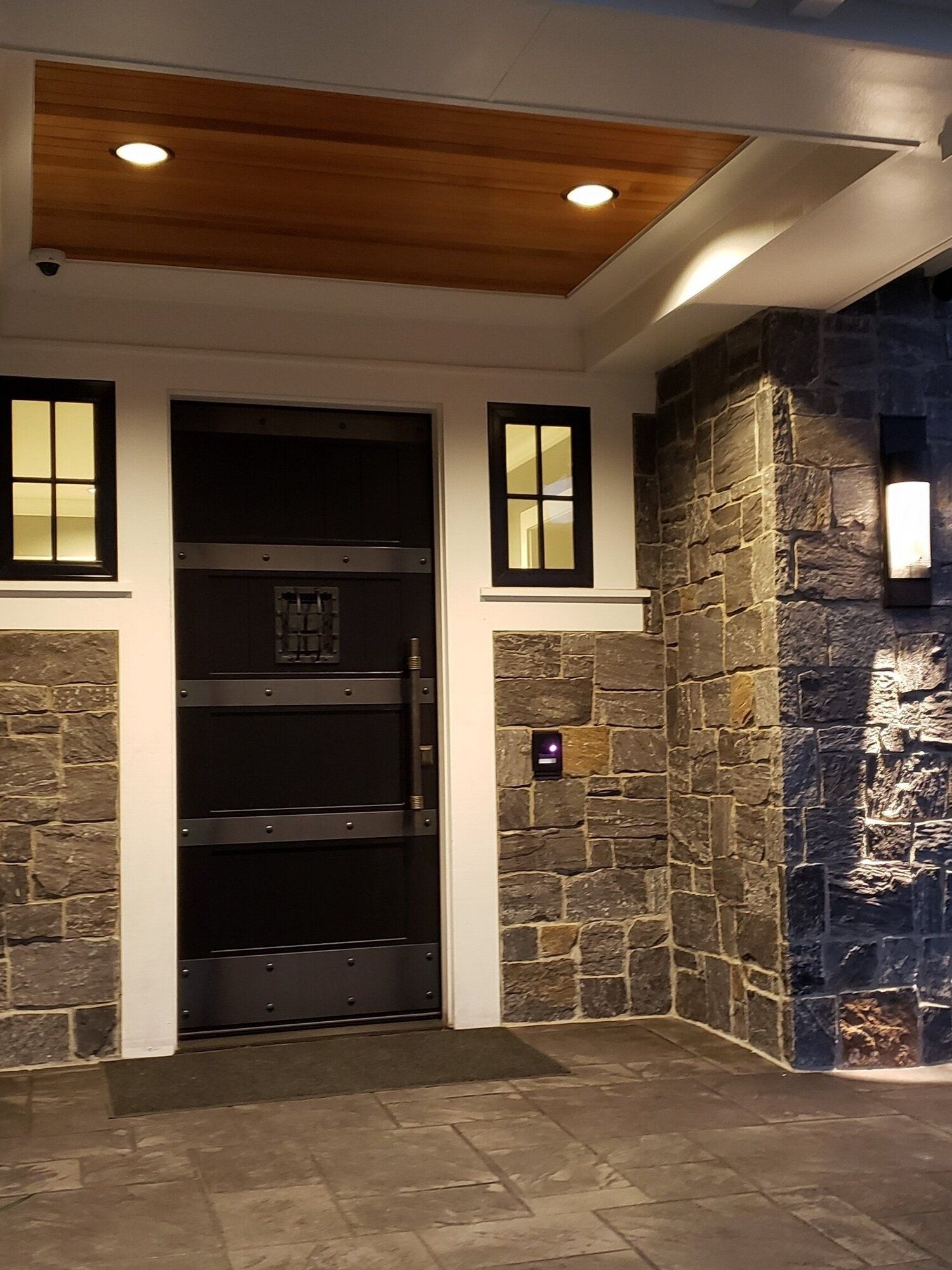 Entrance with stone walls, a dark metal door, small windows, and a wooden ceiling.