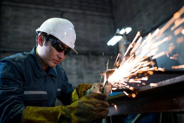 Factory worker welding metal with a torch, showcasing precision in architectural services.