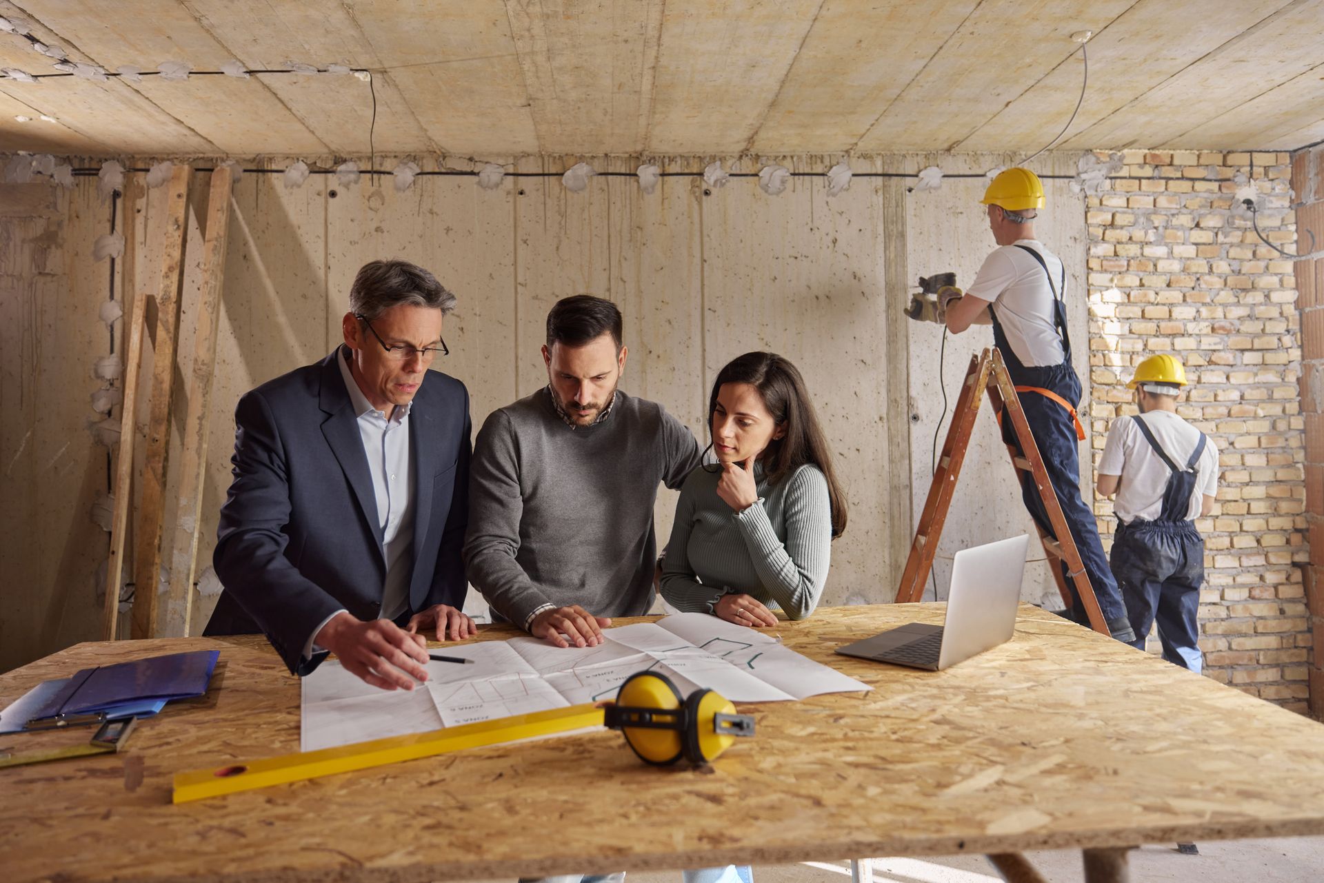 Young couple and their agent examining blueprints at construction site.