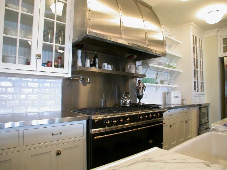 Kitchen with stainless steel range hood over black stove, white cabinets, and white brick backsplash.