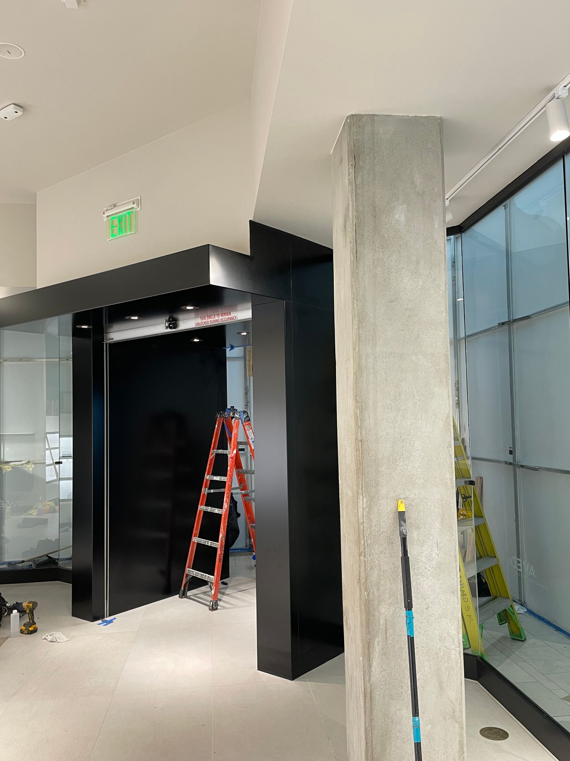 Interior of a commercial space under construction: black door frame, concrete pillar, ladders.