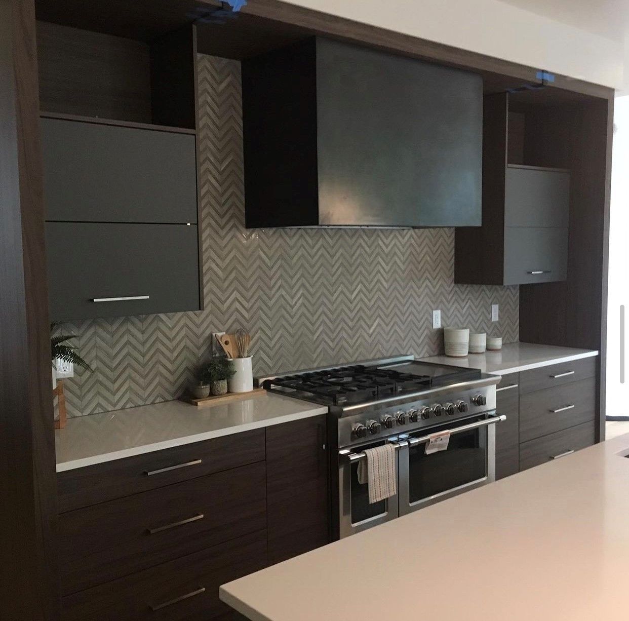 Modern kitchen with dark cabinetry, stainless steel range, light countertops, and herringbone backsplash.