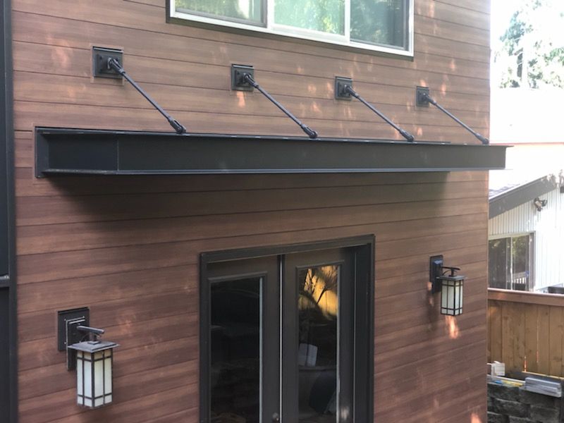 Brown building exterior with a black awning over doors, supported by black angled braces.