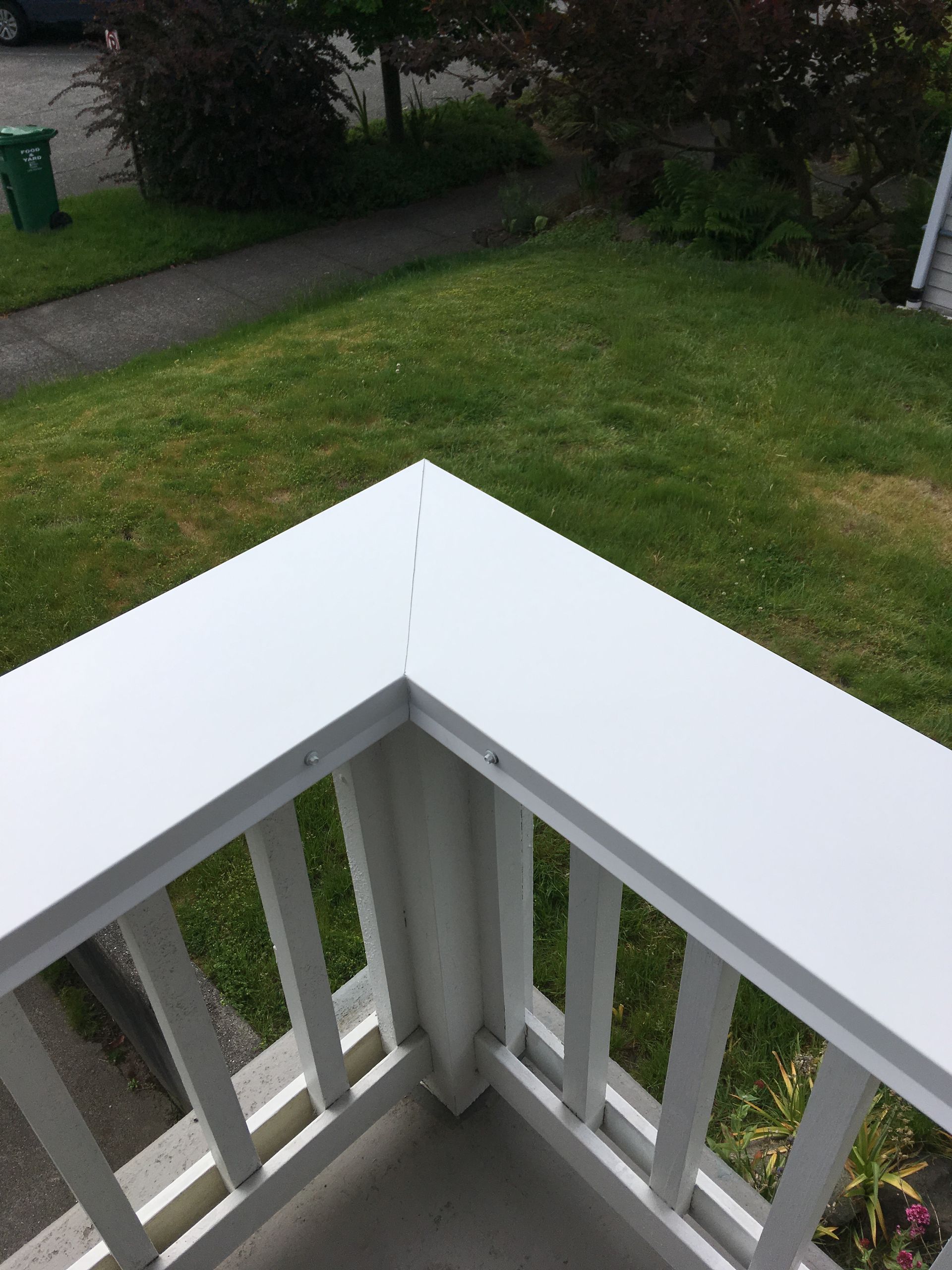 White railing corner with a view of green grass and a sidewalk.