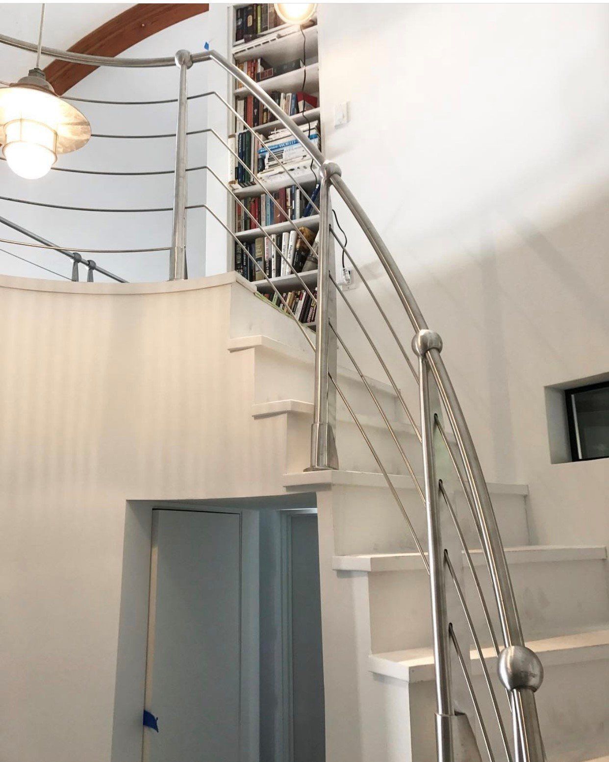 White spiral staircase with steel railing. Bookshelves visible at the top.