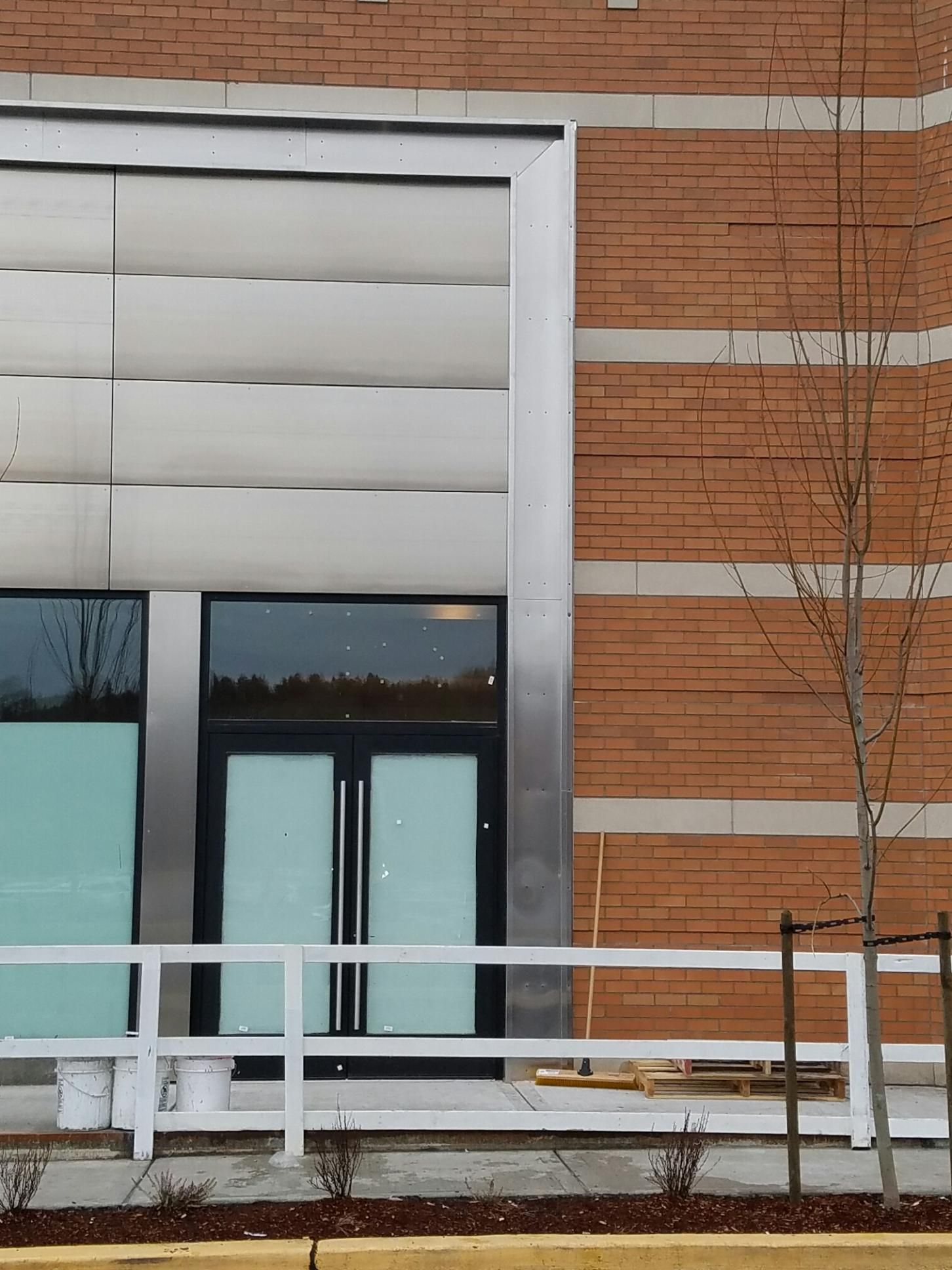 Building facade with a brick wall, metal frame, and light blue glass doors and windows. White railing in foreground.