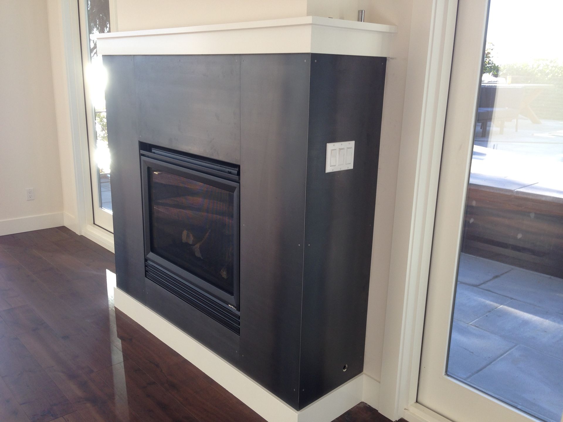 Black fireplace with white trim, set in corner with glass doors and hardwood floors.