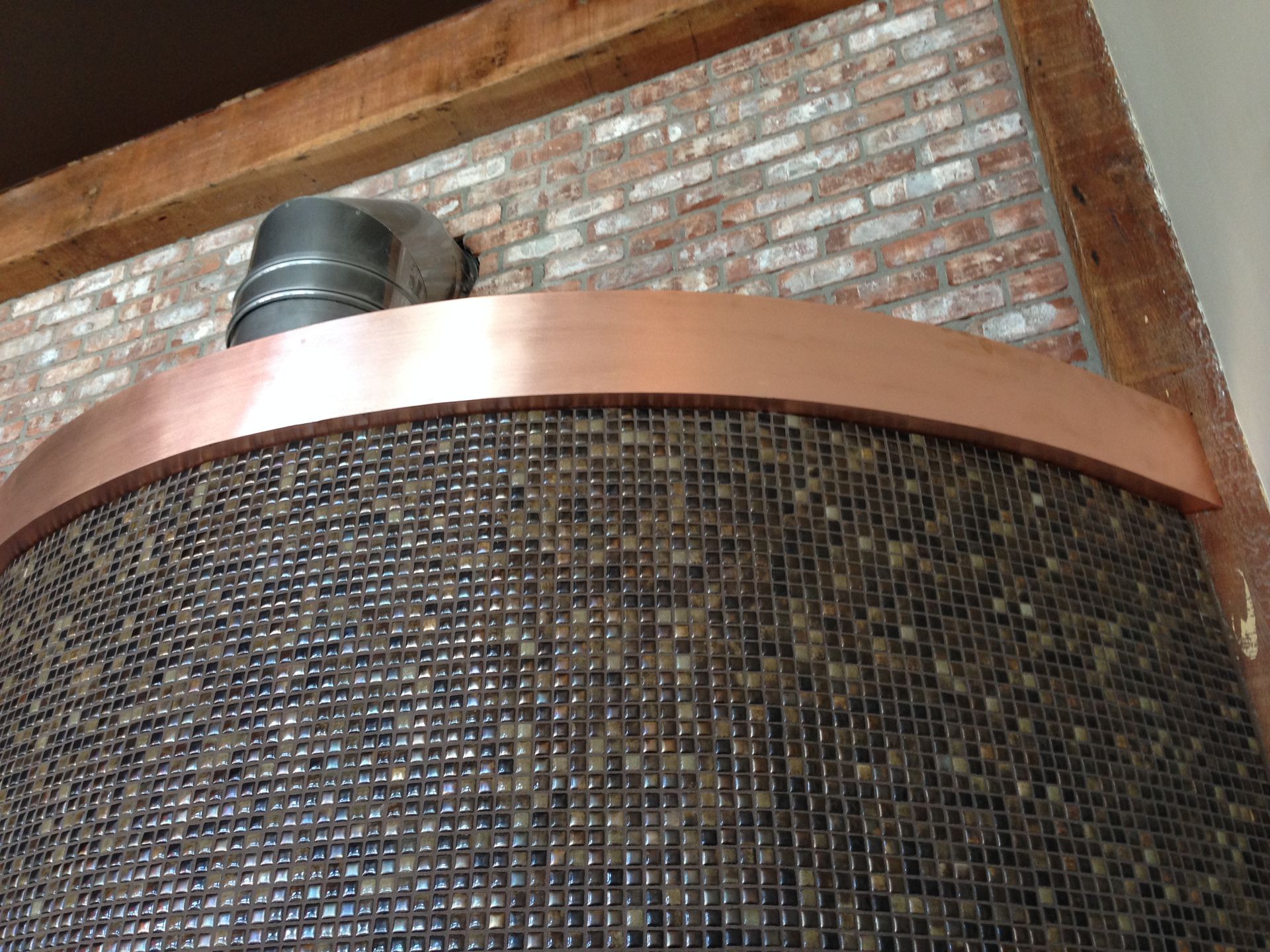 Copper-trimmed, mosaic-tiled structure with a brick background and a metal chimney.