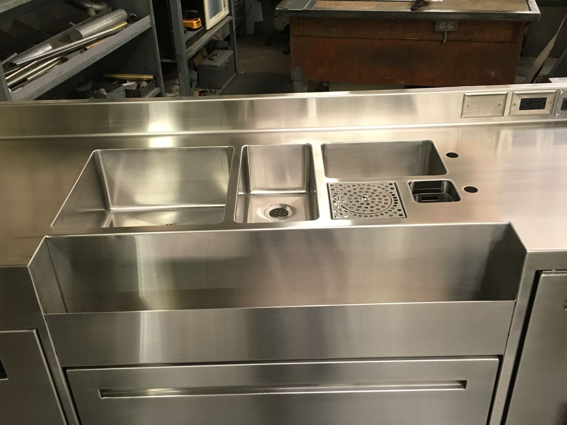 Stainless steel bar workstation with multiple sinks and compartments.