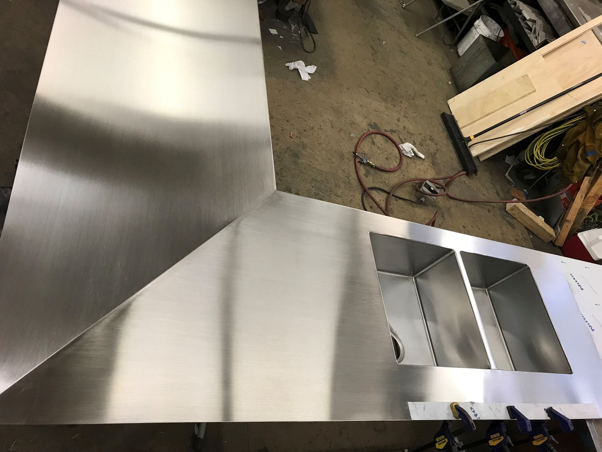 Stainless steel kitchen hood pieces laid out on a workshop floor, showing cuts for sinks.