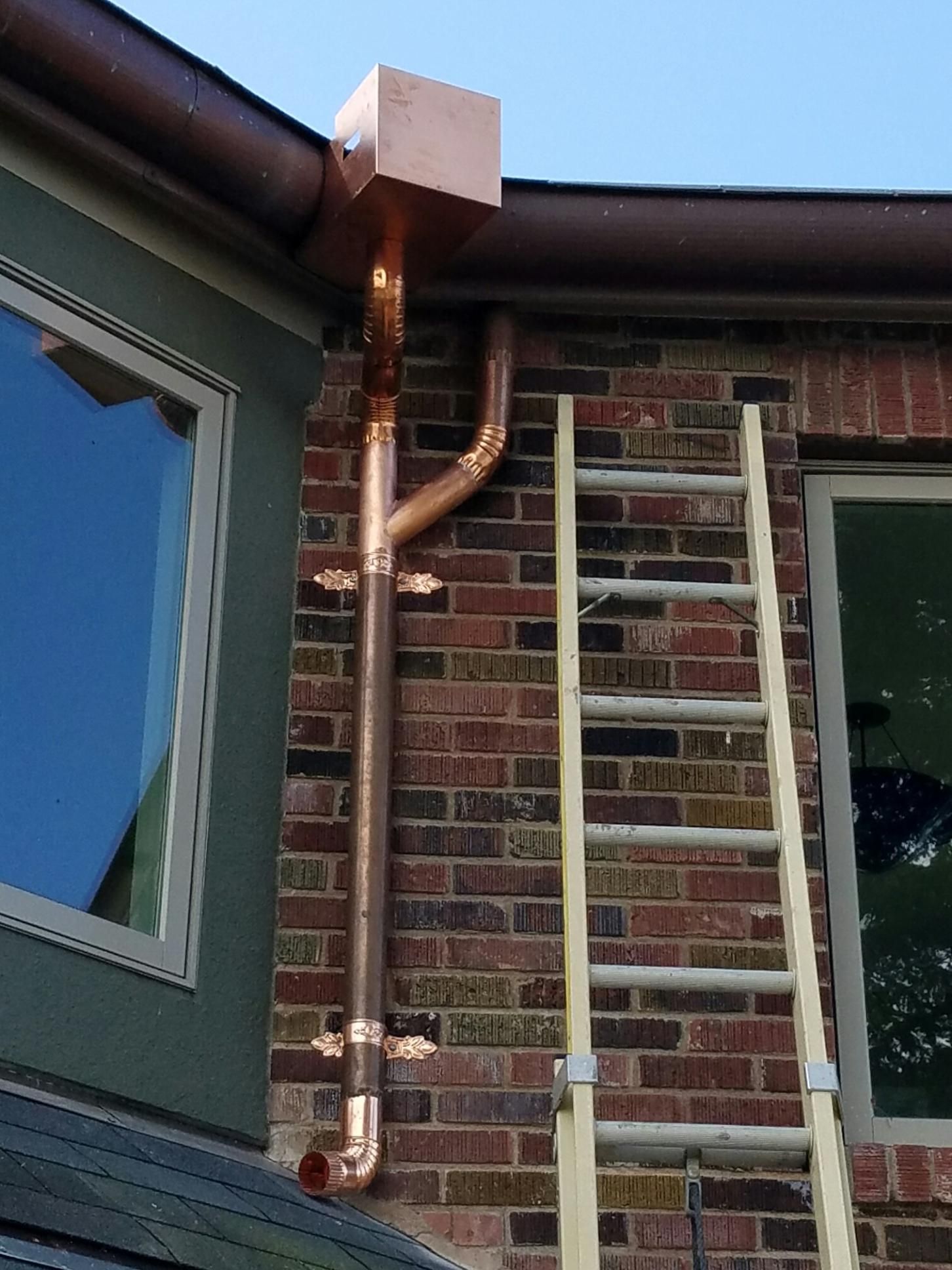 Copper gutter system on brick wall with ladder leaning against it.