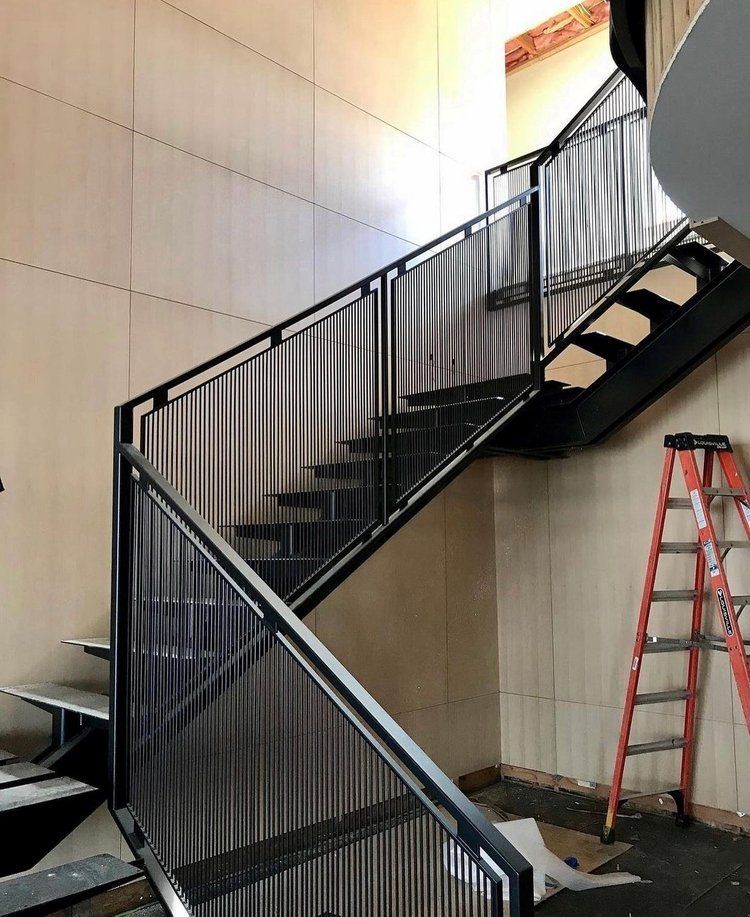 Metal staircase with black railings against light-colored walls; a red ladder leans on the wall.