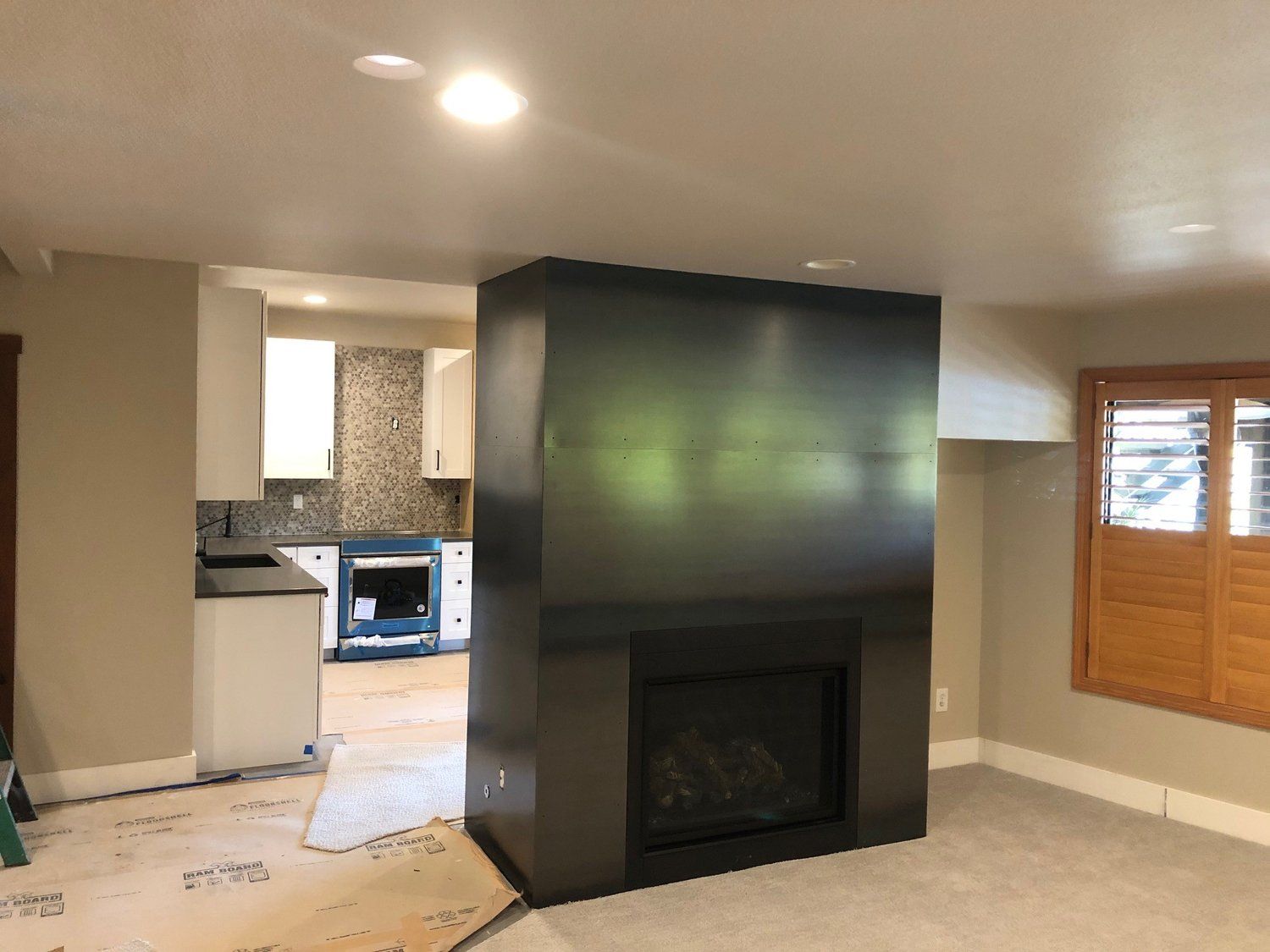 Dark gray fireplace in a beige room, with a kitchen visible in the background.