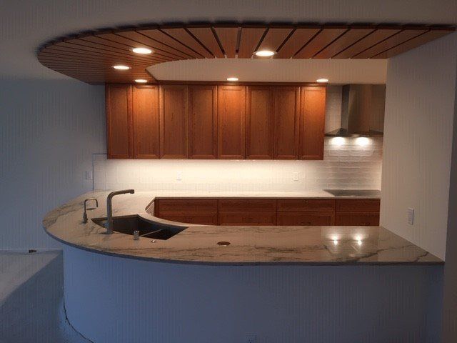 Kitchen with curved countertop, wooden cabinets, and ceiling. Granite countertop, wood ceiling detail.