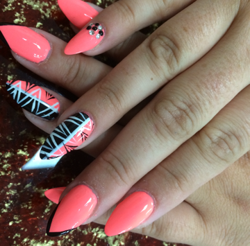 Hands with coral-colored stiletto nails, two adorned with black and white tribal patterns and crystals.