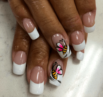 French manicure with two nails featuring bee designs, against a tan skin tone.