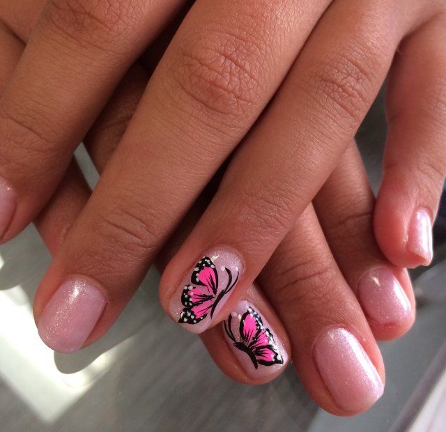 Hands with light pink nail polish, two nails with pink butterfly designs.