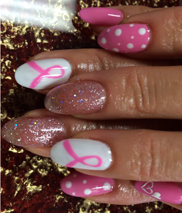 Pink and white nail art with polka dots, glitter, and pink ribbon design for breast cancer awareness.