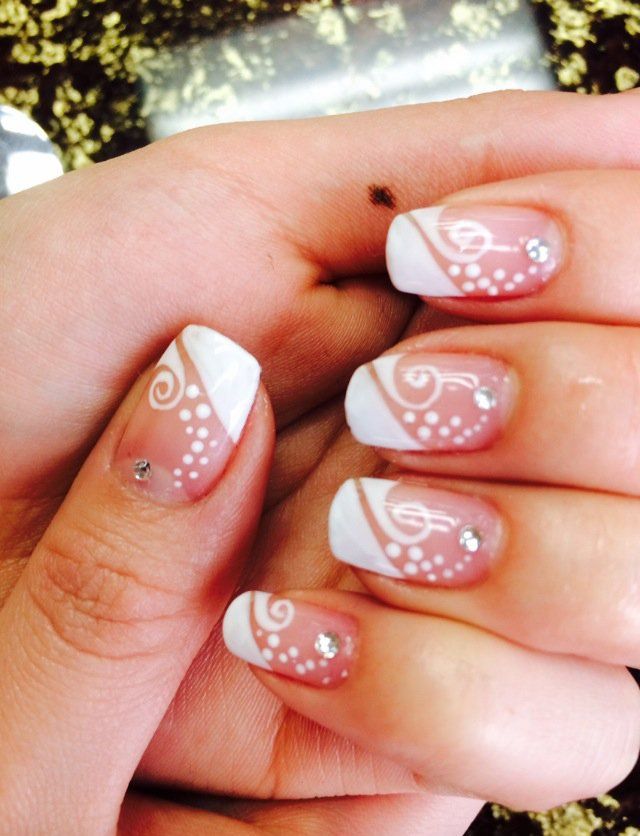 Hand with white and swirl nail art, accented with gems.