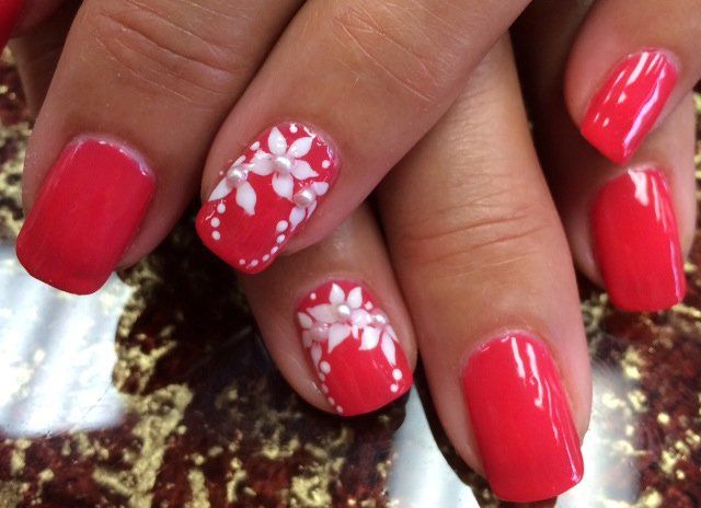 Red and white floral nail art on a person's hand; a red base with white flower design.
