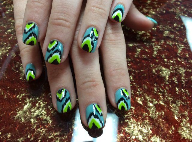 Hands with teal nails featuring a black, neon green, and white zig-zag pattern.