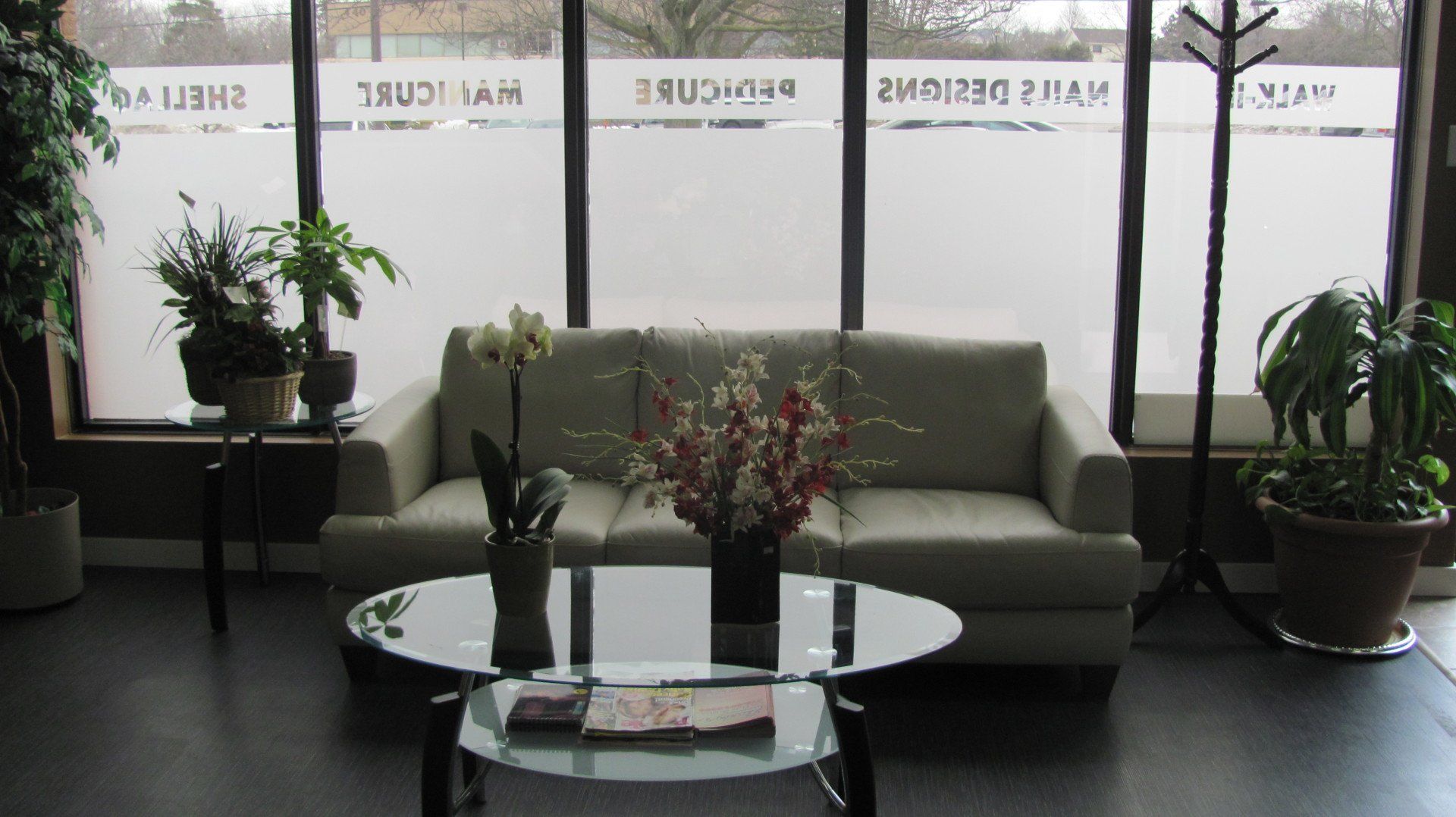 Awaiting area in a salon with a couch, coffee table, plants, and a coat rack by a window.