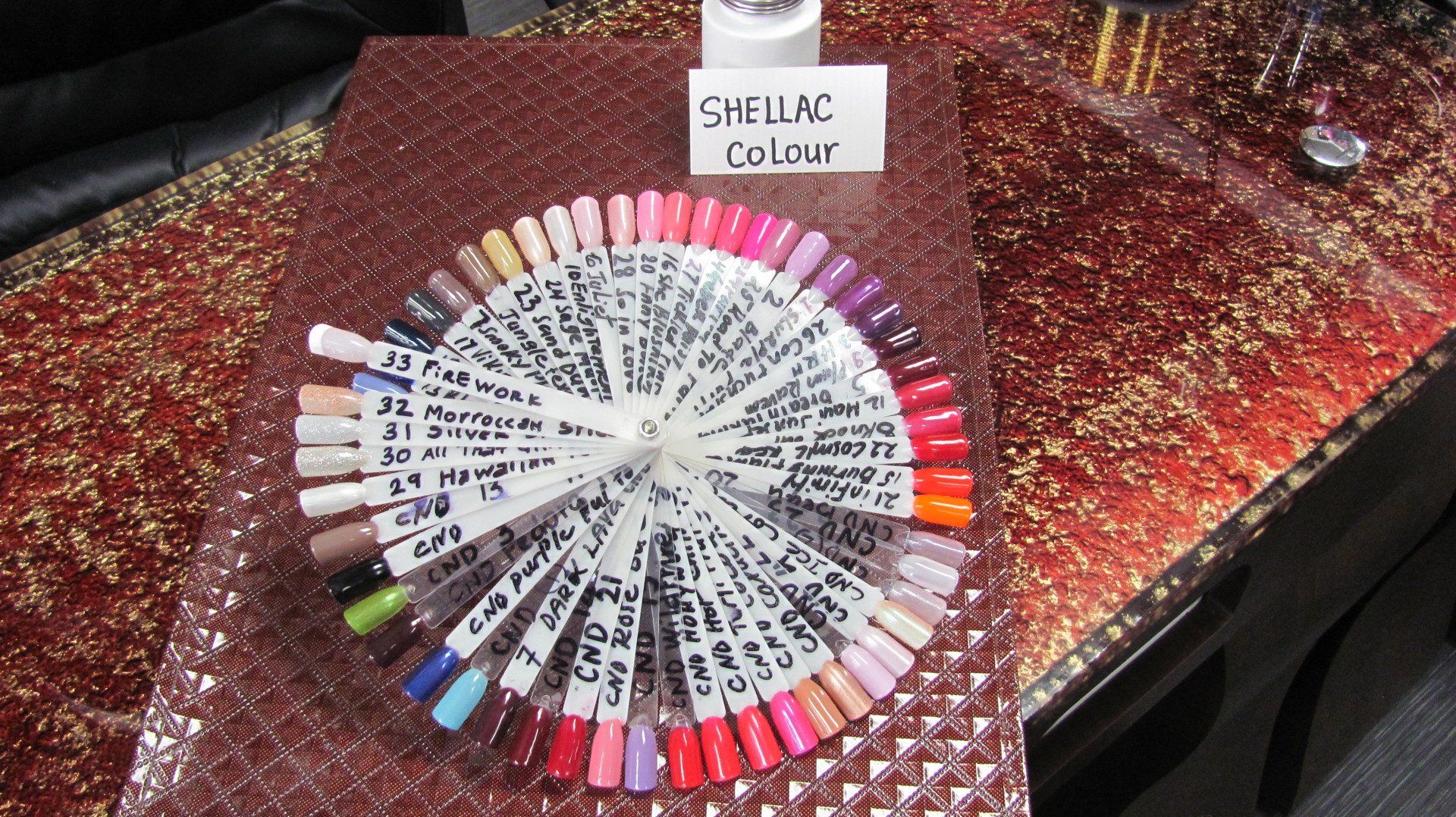 A fan of Shellac nail polish color samples displayed on a glittery surface.