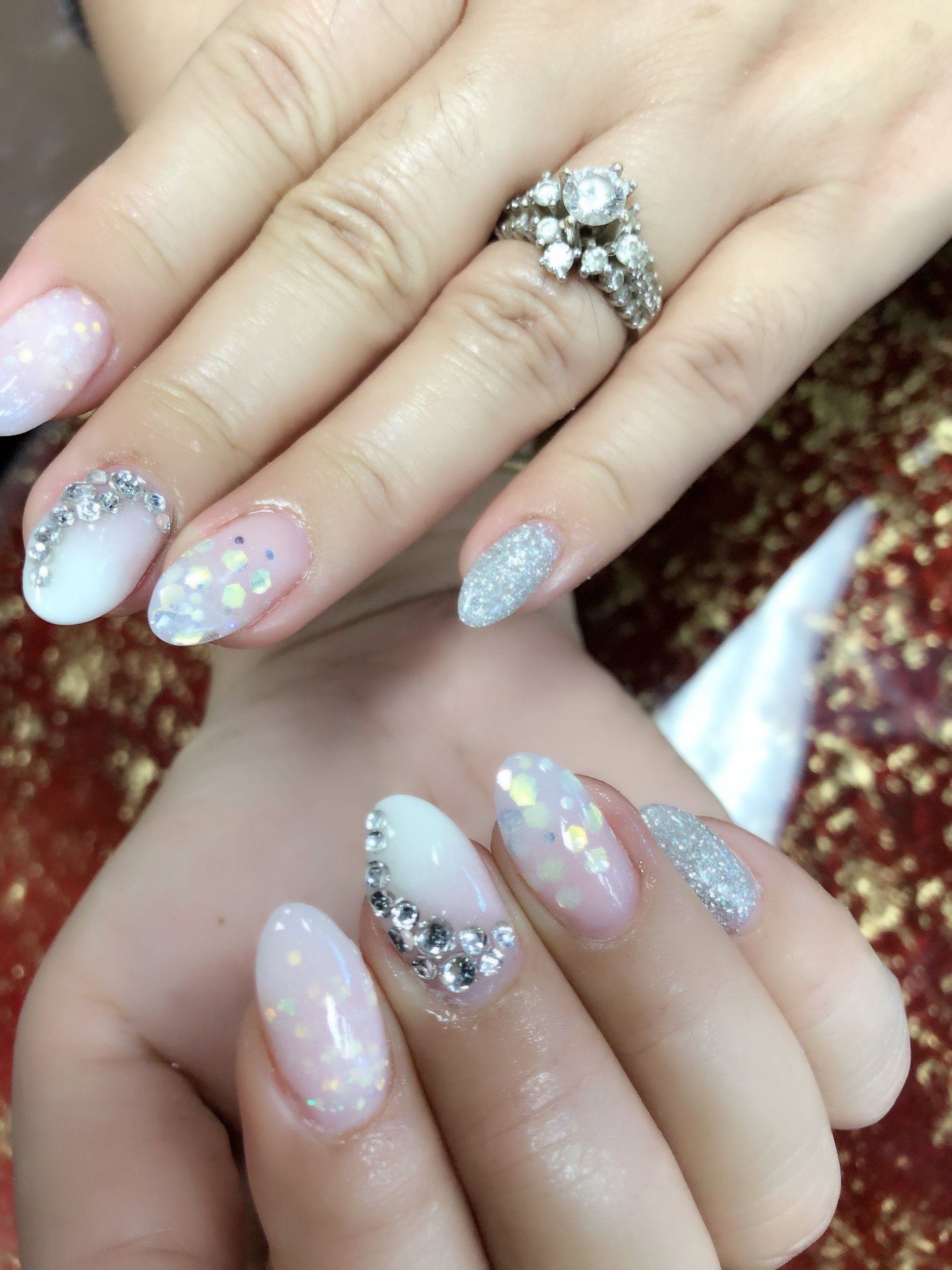 Woman's hands with elegant, sparkly white and glittered nail art. A diamond engagement ring is on one hand.