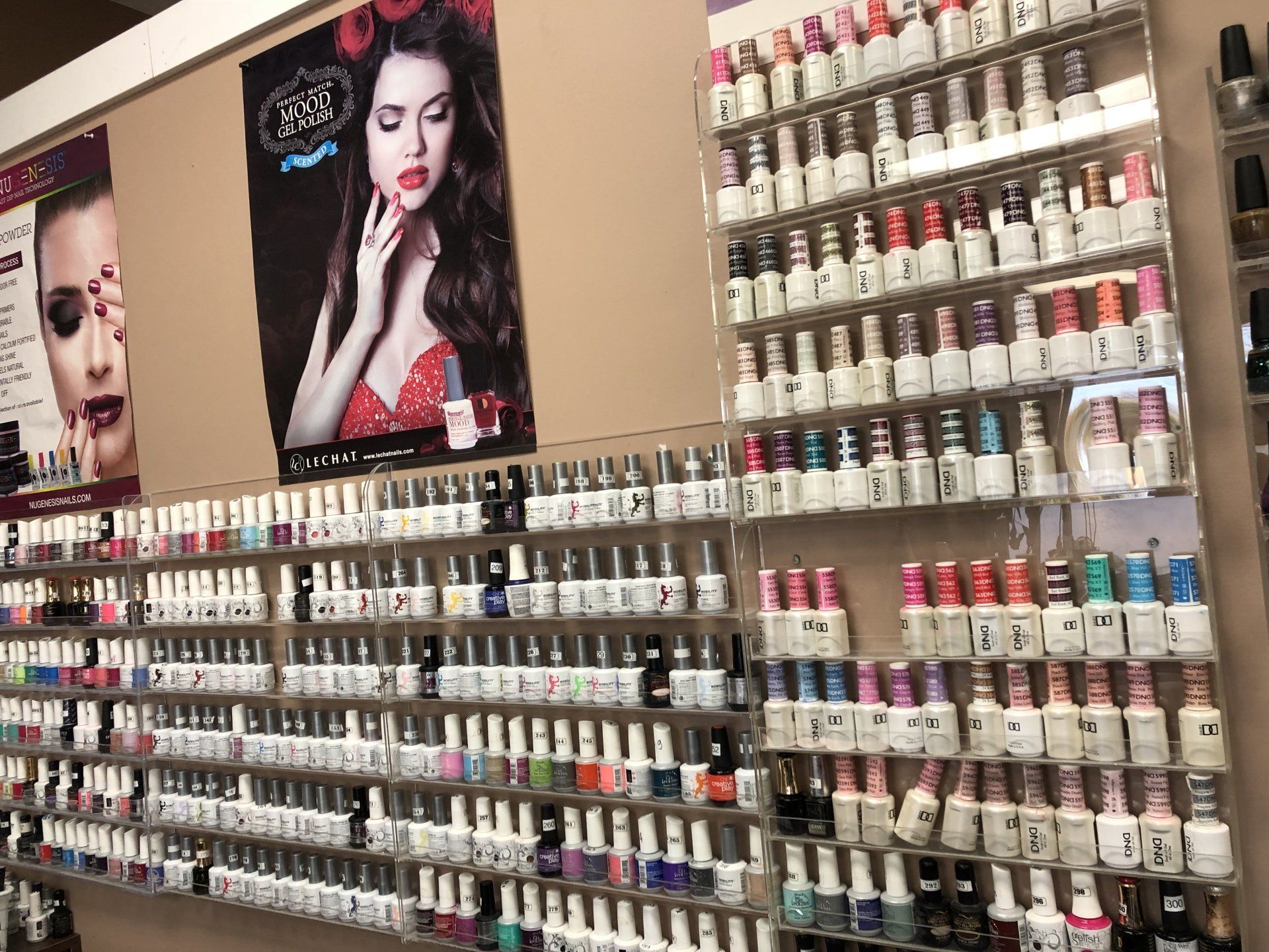 Nail polish display in a salon. Multiple rows of various nail polish colors on shelves, posters of women.