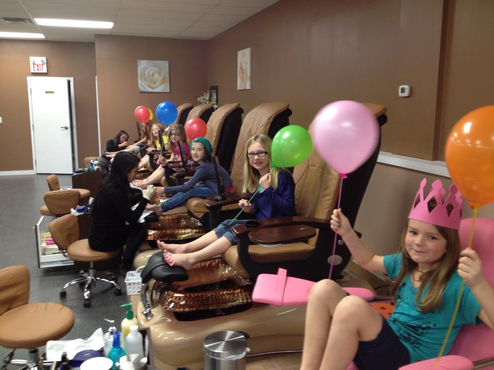 Kids get pedicures at a nail salon, holding colorful balloons.