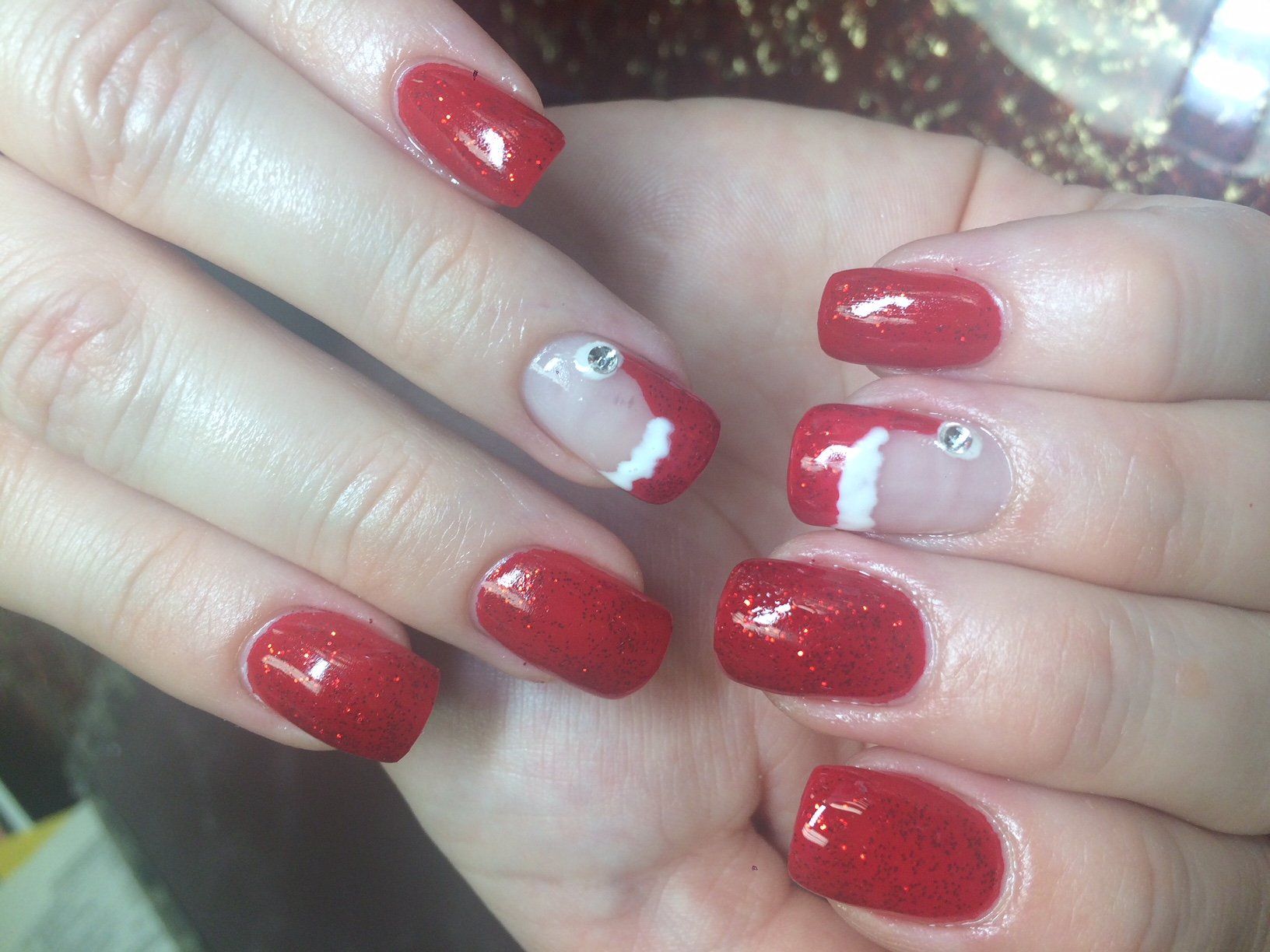 Red glitter nail polish with accent nails featuring white and rhinestones.