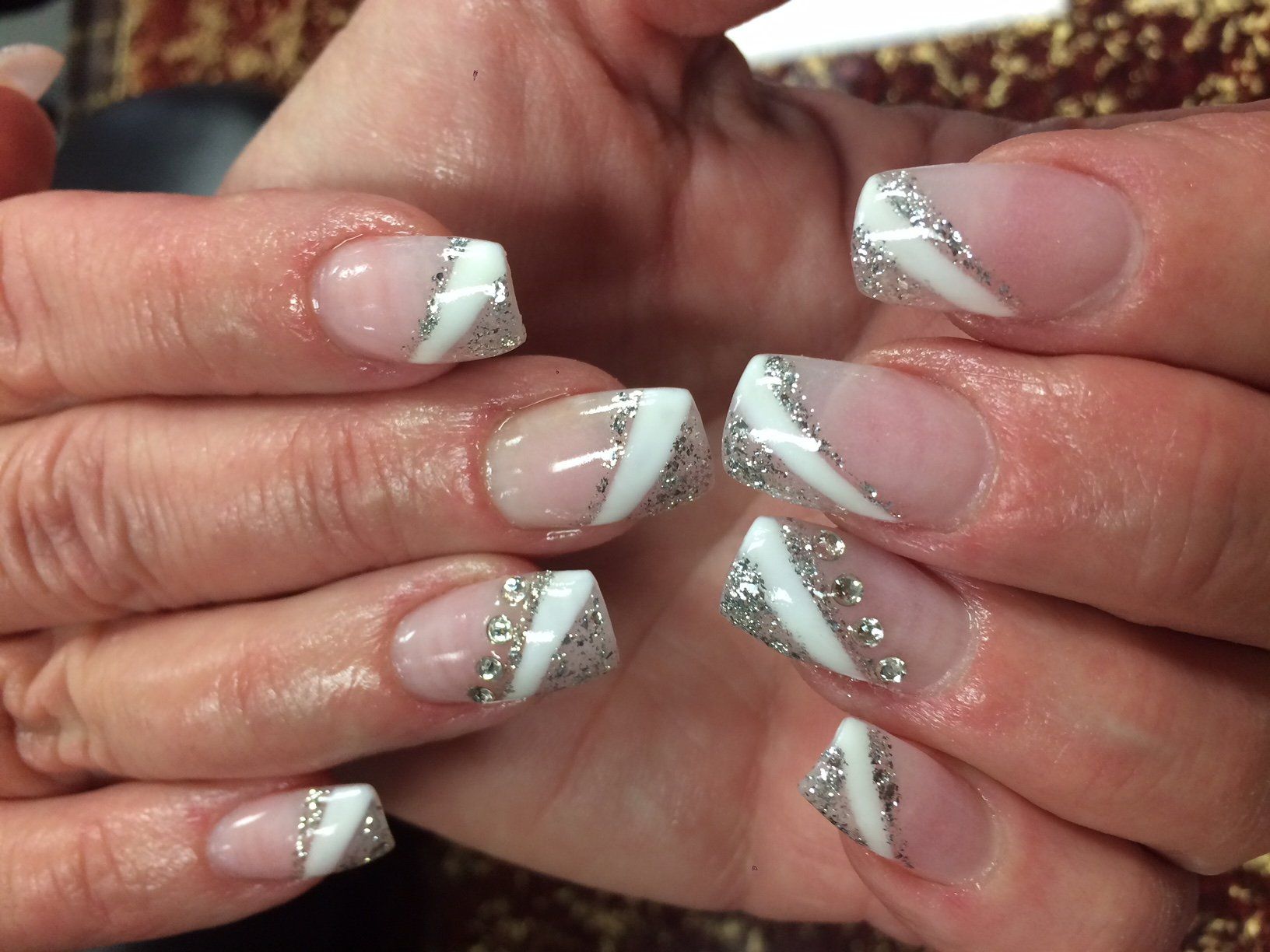 Close-up of hands with square-shaped acrylic nails. White tips and diagonal silver glitter accents on a clear base.