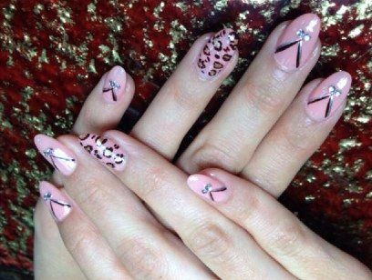 Hands with almond-shaped nails, some pink, decorated with black lines, rhinestones, and a leopard print.