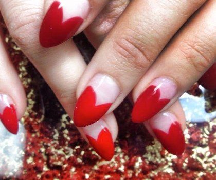 Red heart-shaped nail art on long, pointed nails. A Valentine's Day manicure.