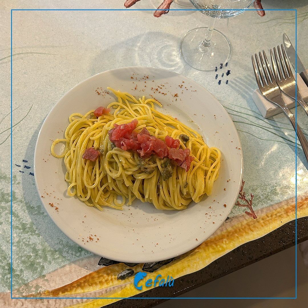 Un piatto bianco con sopra spaghetti e pancetta su un tavolo.
