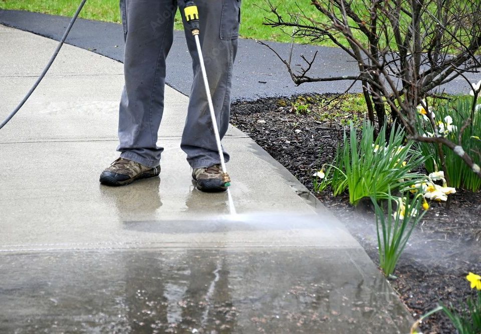 Une personne utilise un nettoyeur haute pression pour nettoyer un trottoir
