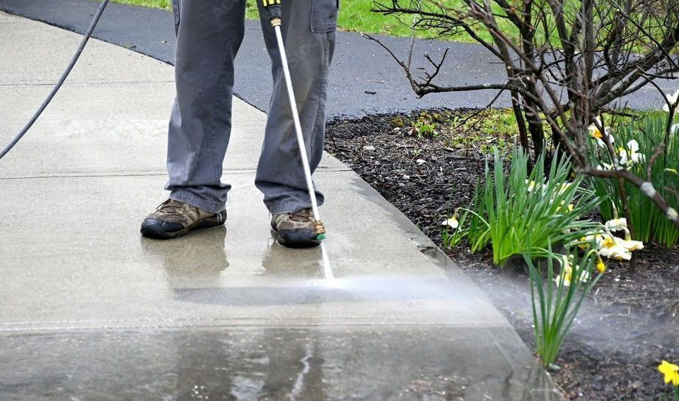 Une personne utilise un nettoyeur haute pression pour nettoyer un trottoir.