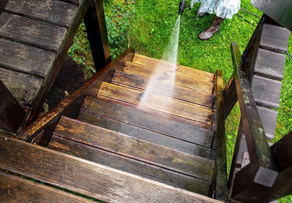 Une personne utilise un nettoyeur haute pression pour nettoyer des escaliers en bois.