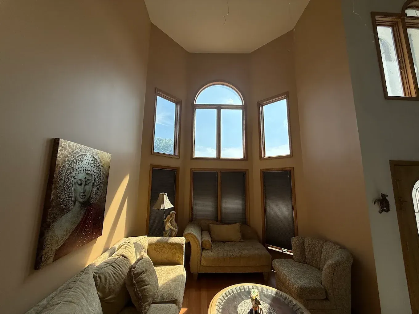 Living room with large windows, sunlight, beige walls, couches, and artwork.