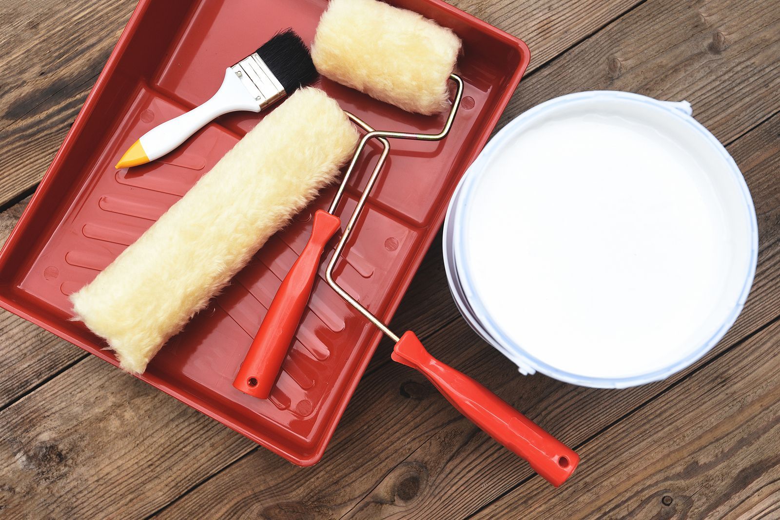 A tray with paint rollers , brushes and a bucket of paint on a wooden table.