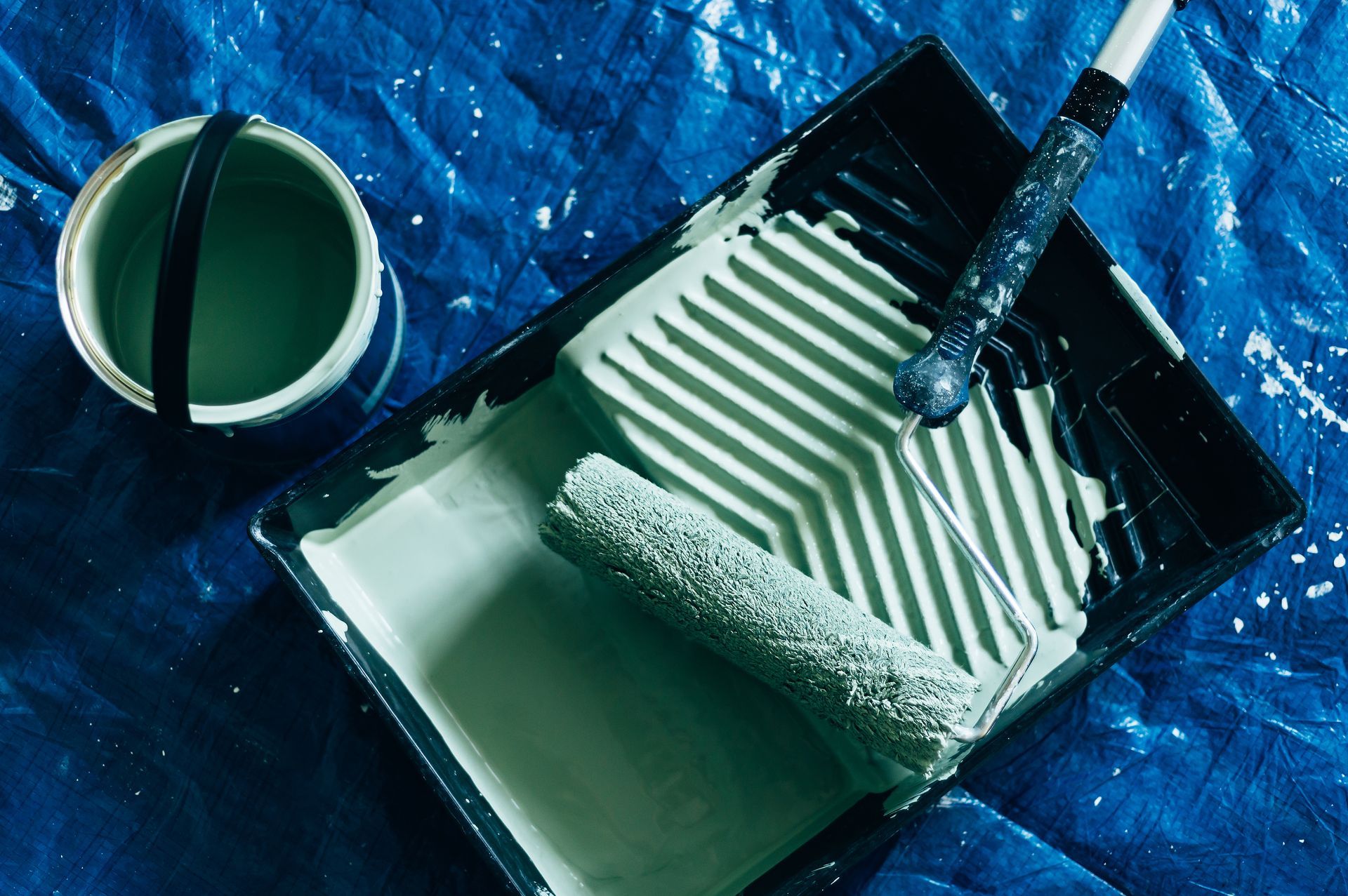 A paint roller is in a paint tray on a blue tarp