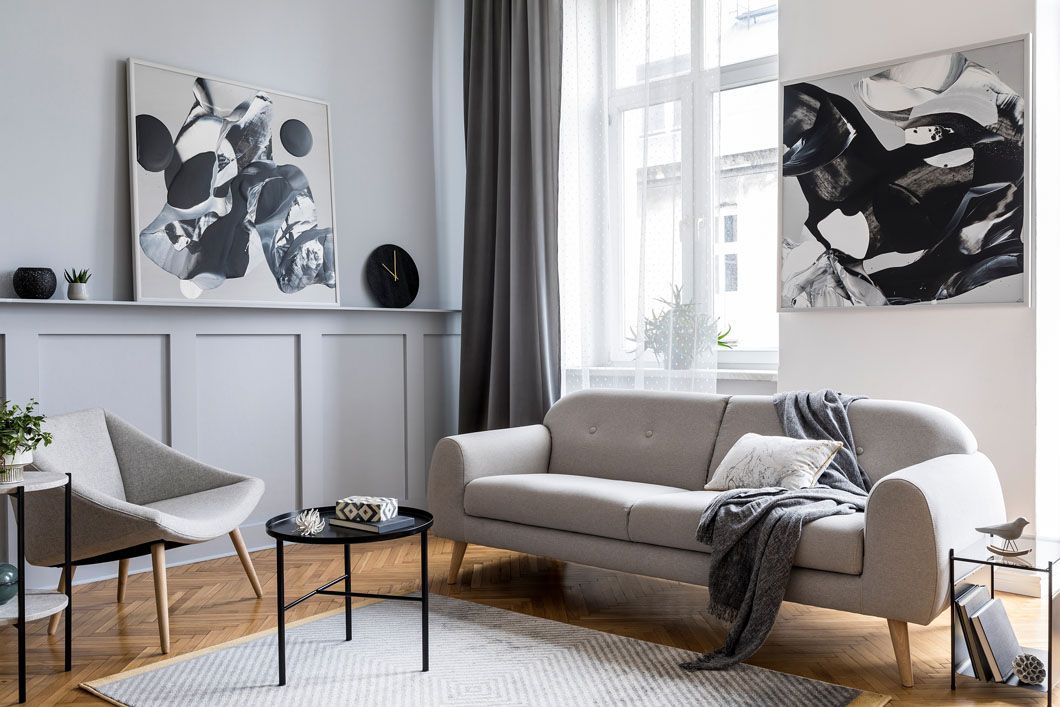 A living room with a couch , chair , table and two paintings on the wall.