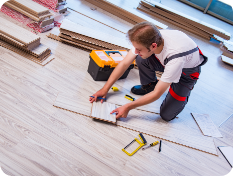 A man is kneeling on the floor while installing a wooden floor.