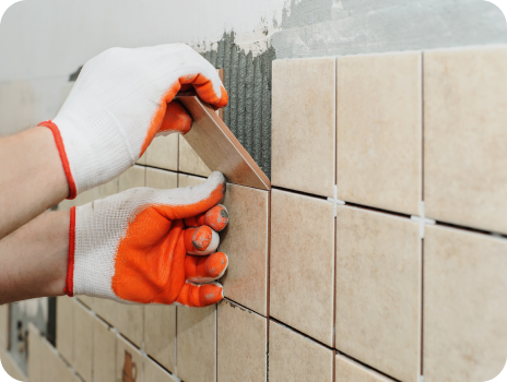A person wearing orange gloves is installing tiles on a wall.