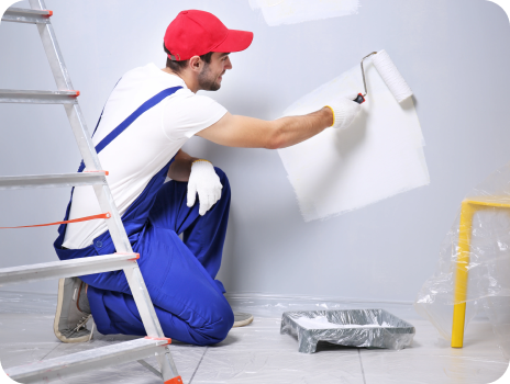 A man is kneeling down while painting a wall with a roller.