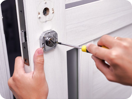 A person is fixing a door lock with a screwdriver.