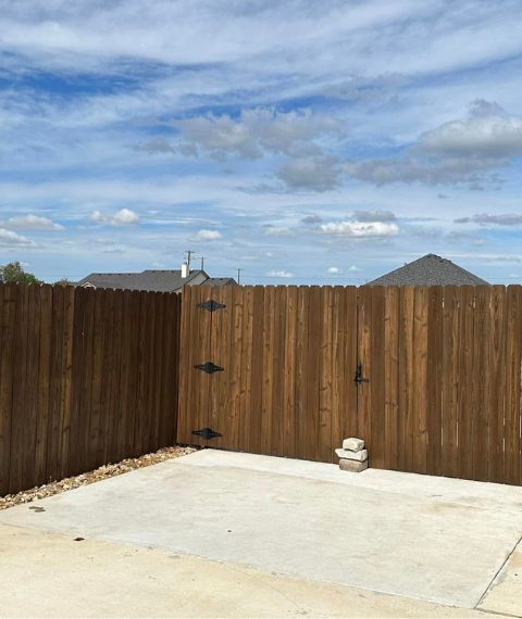 A wooden fence surrounds a concrete area in a backyard